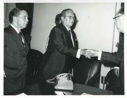 ["Black and white photograph print of President Josip B. Tito shaking hands with an unidentified man as Albert looks on."]