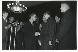 ["Black and white photograph print of Carl Albert shaking hands with members of the Shenyang Acrobatic Troupe. January 13, 1973"]