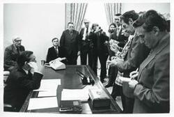 ["Black and white photograph print of Carl Albert seated with Thomas P. O'Neill and Fishbait Miller while reporters ask questions."]