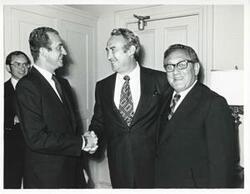 ["Black and white photograph print of King Juan Carlos of Spain shaking hands with Phillip Burton as Henry Kissinger looks on. June 6, 1976"]