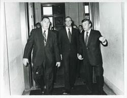 ["Black and white photograph print of Juan Carlos walking down a corridor with unidentified man."]