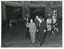 ["Black and white photograph print of Carl Albert, Loise Butler, Helen Newman Tuttle, and others walking at the luncheon in the Speaker's Dining Room for Huang Chen on October 9, 1975"]
