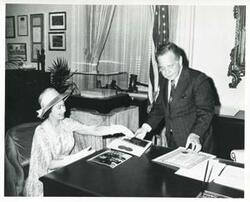 ["Black and white photograph print of Carl Albert and Queen Elizabeth looking at photographs on Albert's desk. 1976"]