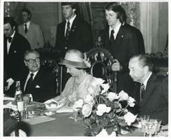 ["Black and white photograph print of Carl Albert, Queen Elizabeth, and Nelson Rockefeller seated at a dinner table."]