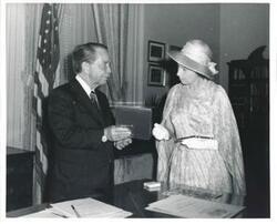 ["Black and white photograph print of Carl Albert and Queen Elizabeth looking at pictures at Albert's desk."]