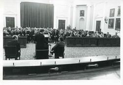 ["Black and white photograph print of Carl Albert and Gerald R. Ford seated in a room with several other men at an unknown function, and Henry Kissinger is also shown."]