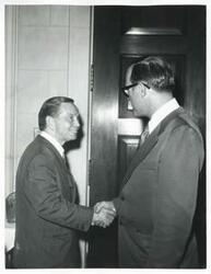 ["Black and white photograph print of Carl Albert shaking hands with an unidentified man."]