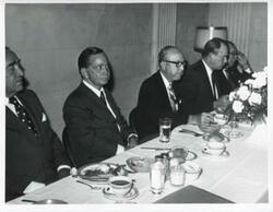 ["Black and white photograph print of Carl Albert, Henry Bellmon, and others seated at a dinner table."]