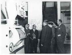 ["Black and white photograph print of several men (individual names on the back of the photo) at a modern bread factory in Bogota, Columbia."]