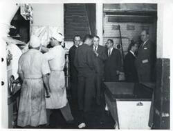 ["Black and white photograph print of Carl Albert with several others (individual names on the back of photograph) at a modern bread factory in Bogota, Columbia."]