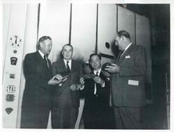 ["Black and white photograph print of Carl Albert with several others (individual names on the back of photograph) at a modern bread factory in Bogota, Columbia."]
