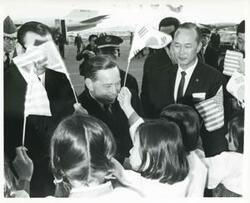 ["Black and white photograph print of Carl Albert standing with several Korean children who are waving Korean and American flags. This was taken during the trip to Korea."]