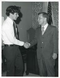 ["Black and white photograph print of Carl Albert shaking hands with an unidentified man's hand."]