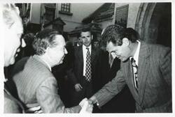["Black and white photograph print of Carl Albert shaking hands with an unidentified man while others looking on the House delegation trip. August 1975"]