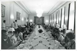 ["Black and white photograph print of a large group of people seated at a dinner table."]