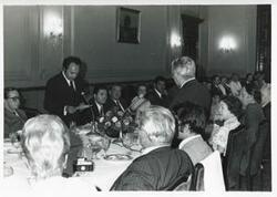 ["Black and white photograph print of Carl Albert and Mary Albert seated at a dinner table with several others. House delegation trip. August 1975"]