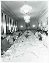 ["Black and white photograph print of a large group of people seated at a dinner table House delegation trip. August 1975"]