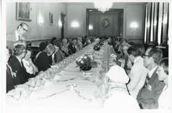 ["Black and white photograph print of a large group of people seated at a dinner table House delegation trip. August 1975"]
