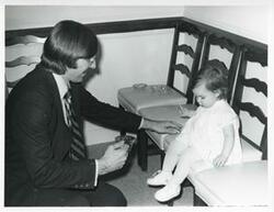 ["Black and white photograph print of an unidentified man playing with a small child at Carole Howard's farewell party."]