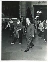 ["Black and white photograph print of Carl Albert and several people walking in the lobby of a building."]