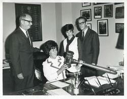 ["Black and white photograph print of Charles Ward and Mike Reed with two unidentified woman at Carl Albert's desk."]