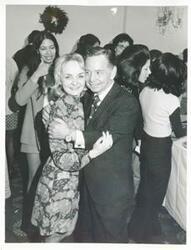 ["Black and white photograph print of Polly Ritter hugging Carl Albert at the Staff Christmas Party. Sherry Tonubbee Stewart is standing in the background, 1971"]