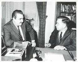 ["Black and white photograph print of Carl Albert seated and talking with an unidentified man at his desk."]