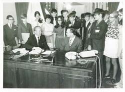 ["Black and white photograph print of Carl Albert seated at his desk. Behind him is a large group of young people dubbed the quiz-kids."]