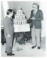 ["Black and white photograph print of Carl Albert and an unidentified man standing beside a model of the Capitol made with flowers."]