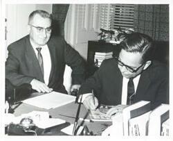 ["Black and white photograph print of Carl Albert signing a cover of Time magazine on which he appears."]
