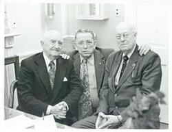 ["Black and white photograph print of three unidentified men seated and posing together."]