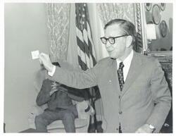 ["Black and white photograph print of Carl Albert standing in his office holding an unidentified object."]