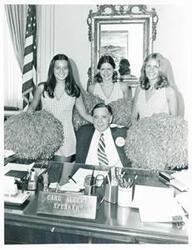 ["Black and white photograph print of Carl Albert seated at his desk; behind him are Stanford University cheerleaders L. to R. - Terry Elms, Toni Hunter, and Bonnie McCall. September 16, 1975"]