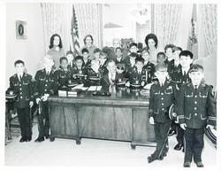 ["Black and white photograph print of Carl Albert seated at his desk and posing with several young boys from Linton Hall."]