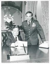 ["Black and white photograph print of Carl Albert and Robinson Risner posing for a picture at Albert's desk. November 1974"]