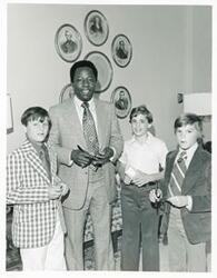 ["Black and white photograph print of Hank Aaron signing autographs for three young boys."]