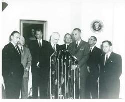 ["Black and white photograph print of Mike Mansfield, Harry F. Byrd, John W. McCormack, Hubert H. Humphrey, Lyndon B. Johnson, Wilbur D. Mills, and Carl Albert standing in front of microphones. Same as photo 1698"]