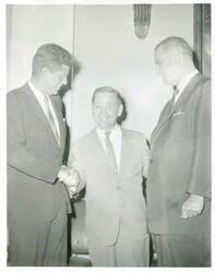 ["Black and white photograph print of Carl Albert shaking hands with John F. Kennedy as an unidentified man looks on."]
