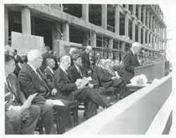 ["Black and white photograph print of Carl Albert, John F. Kennedy, Earl Warren, with others at the Rayburn building dedication. John W. McCormack is speaking."]