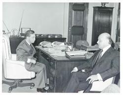 ["Black and white photograph print of Carl Albert seated at his desk. Mayor Aliotas is seated next to him."]