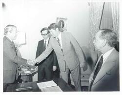 ["Black and white photograph print of John Rhodes shaking hands with an unidentified man as Carl Albert looks on."]
