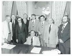 ["Black and white photograph print of Carl Albert is seated at his desk. Behind him is Thomas E. Morgan and several unidentified men."]