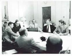 ["Black and white photograph print of Thomas E. Morgan, Henry Reuss, and several other men seated around a round table."]