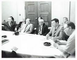 ["Black and white photograph print of Melvin Price, Thomas E. Morgan, and several other men seated at a round table."]