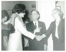 ["Black and white photograph print of Lady Bird Johnson shaking hands with an unidentified woman as Carl Albert looks on."]