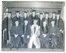 ["Black and white photograph print of several unidentified men posing for a photo. They are all wearing mortar boards and robes."]