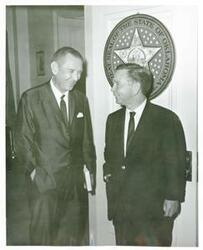 ["Black and white photograph print of Carl Albert standing and talking with an unidentified woman."]