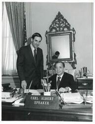 ["Black and white photograph print of Carl Albert seated at his desk. Standing behind him is Duke Ligon, director of the Oil and Gas Division of the Department of the Interior."]