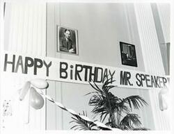 ["Black and white photograph print of a banner reading, Happy Birthday Mr. Speaker. There are two photos above the banner of Mr. Albert."]