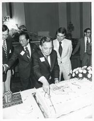 ["Black and white photograph print of Carl Albert cutting his birthday cake."]